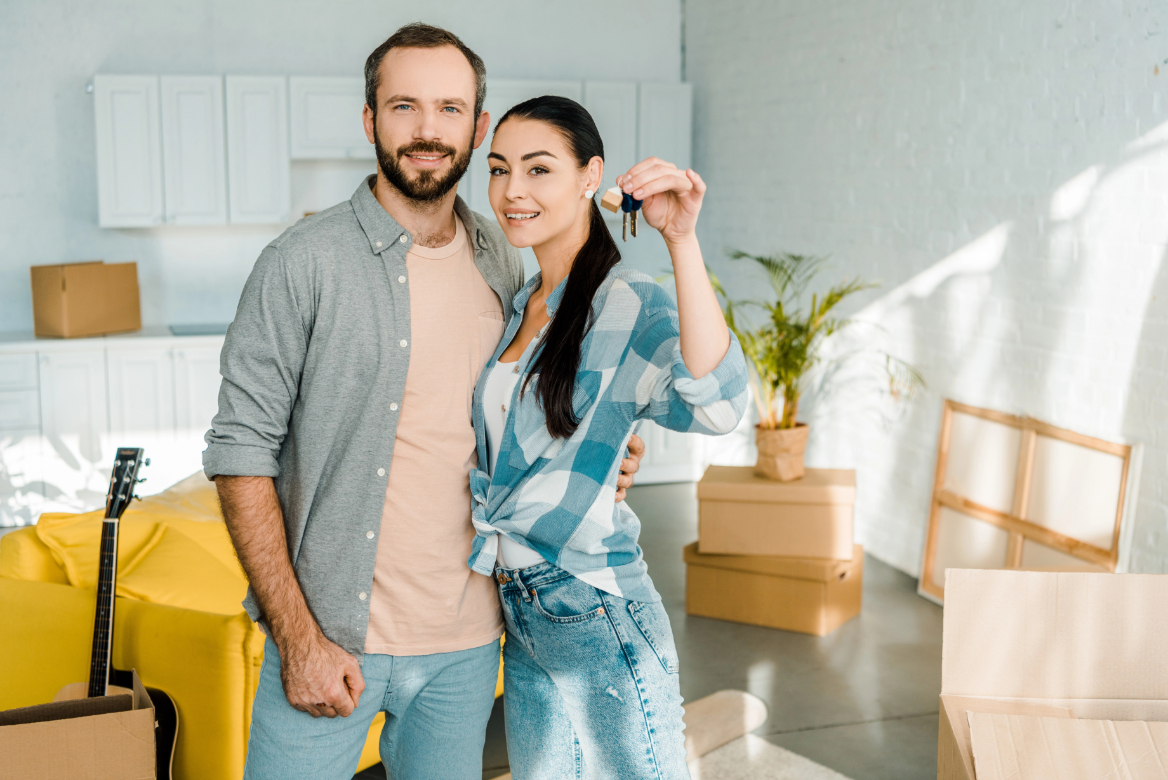 Smiling couple looking at camera and wife holding keys from new house, moving concept Smiling couple looking at camera and wife holding keys from new house, moving concept